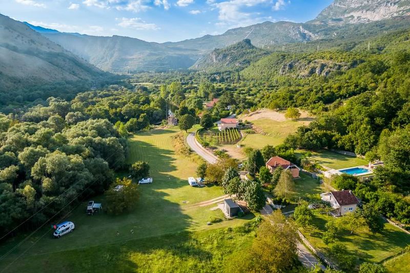 Vazdušni snimak eko kampa Ilijin Vir u zelenoj dolini okruženoj planinama, sa k amperima na livadi i bazenom